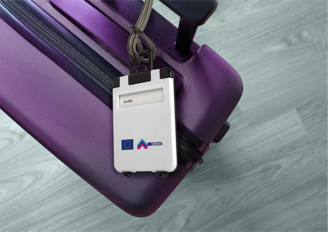 A purple suitcase with a blank name tag displaying a logo on a grey floor.