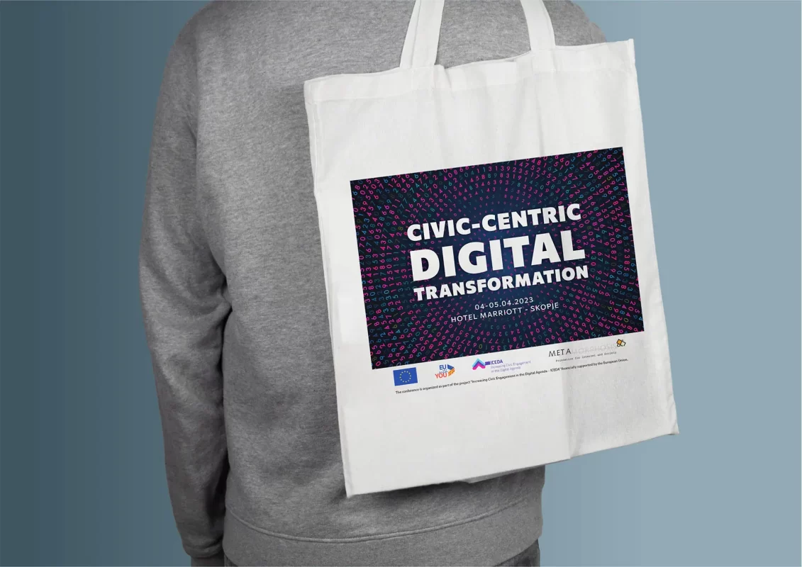 Person holding a white tote bag with "CIVIC-CENTRIC DIGITAL TRANSFORMATION" event details.