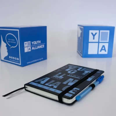 Notebook with "THE YOUTH VOICE" text, blue pen, and branded cubes for Youth Alliance.