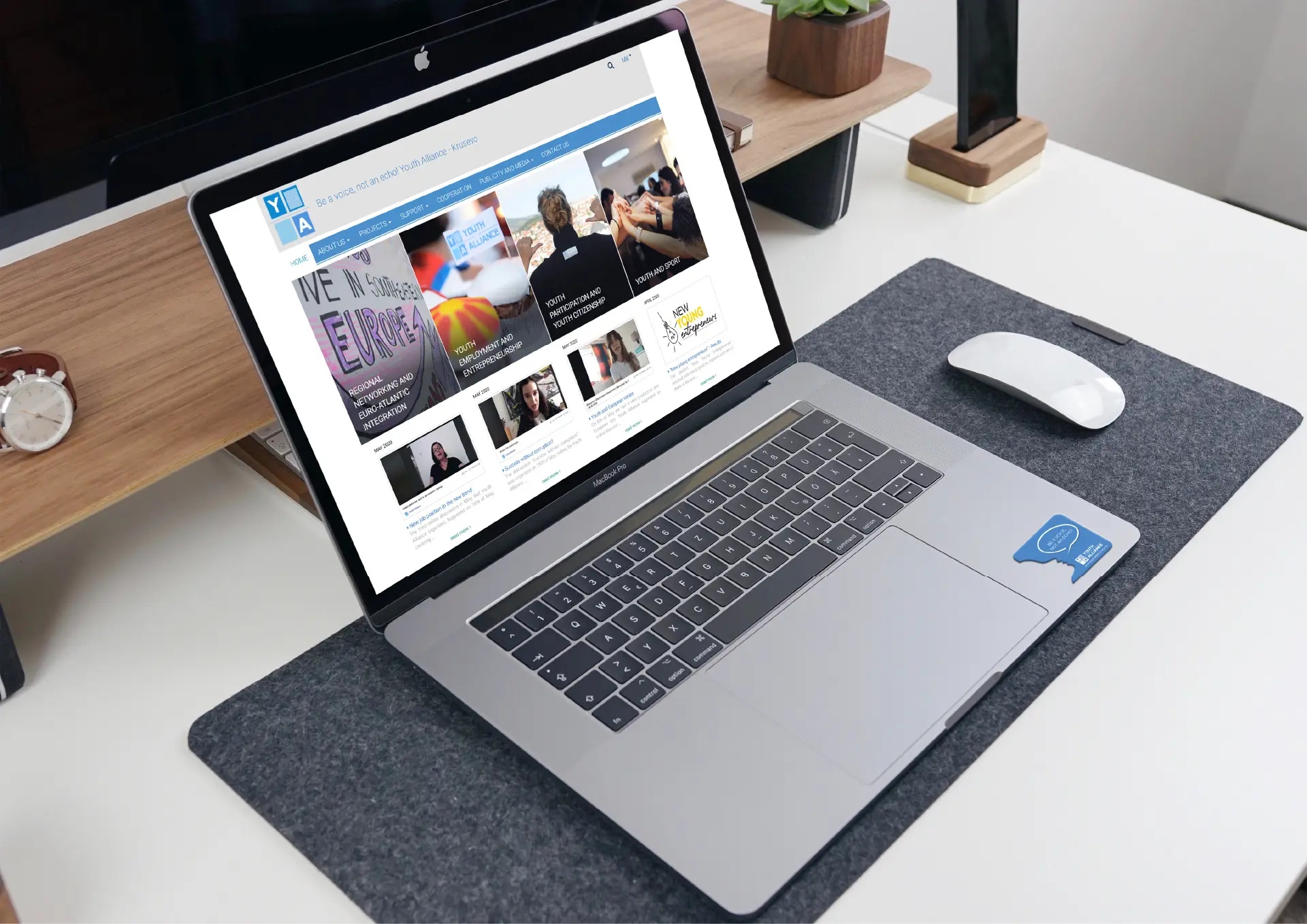 Laptop on desk with mouse and wristwatch, displaying a webpage.