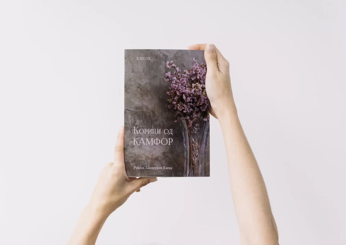 Hands holding a book with a floral cover design against a white background.