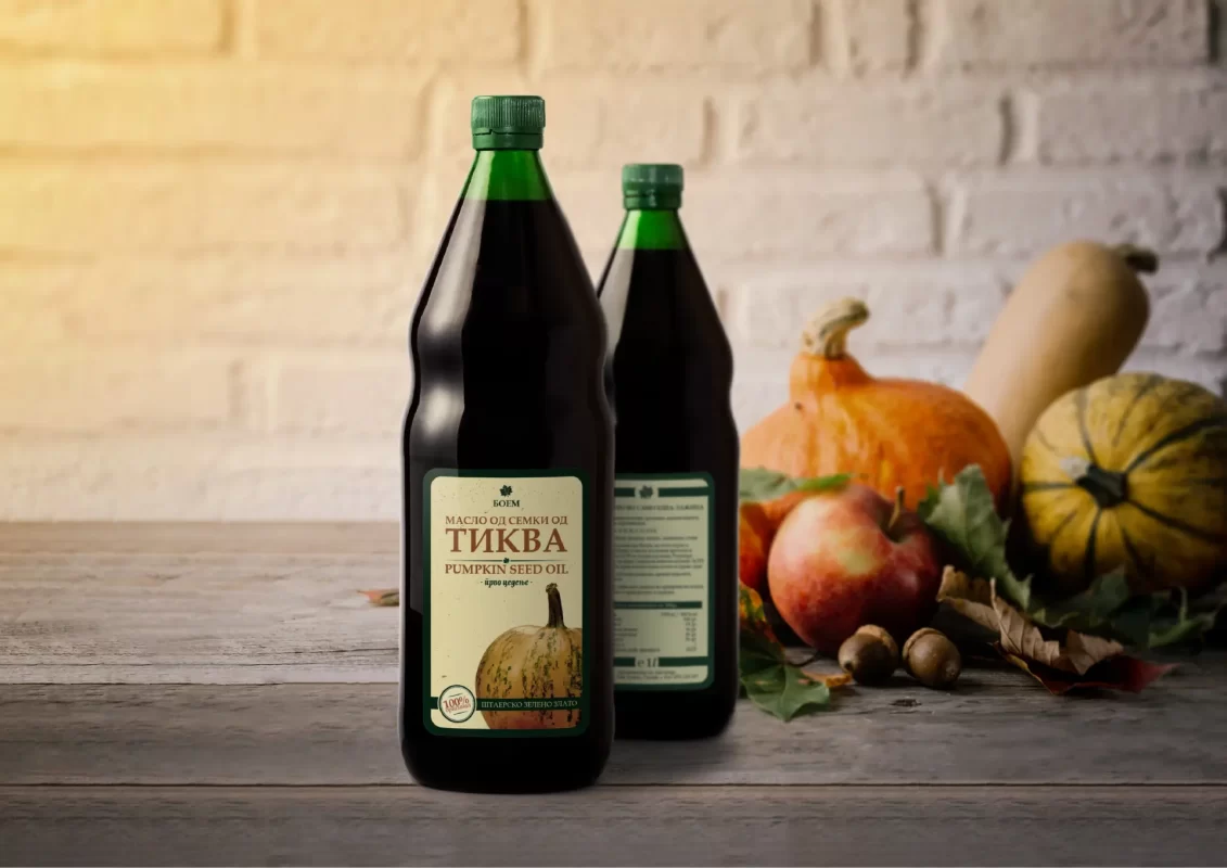 Two bottles of pumpkin seed oil with pumpkins and apples in the background.