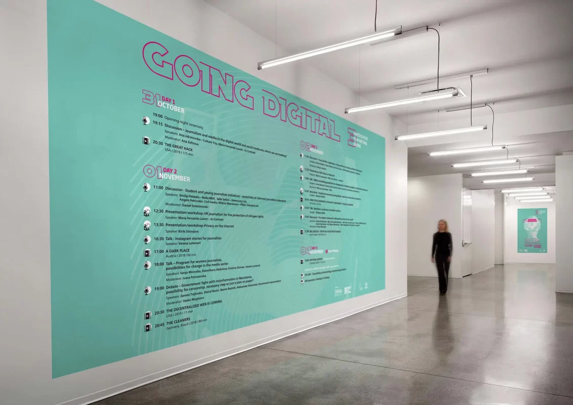 A large teal event schedule titled "GOING DIGITAL" on a wall in a modern hallway.