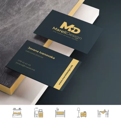 Business cards for "MareliDesign" with gold text on black background displayed on a gray surface.