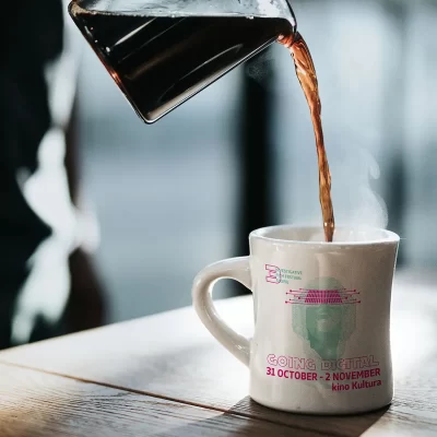 Coffee being poured into a mug with "GOING DIGITAL" text, steam rising, on a wooden surface.