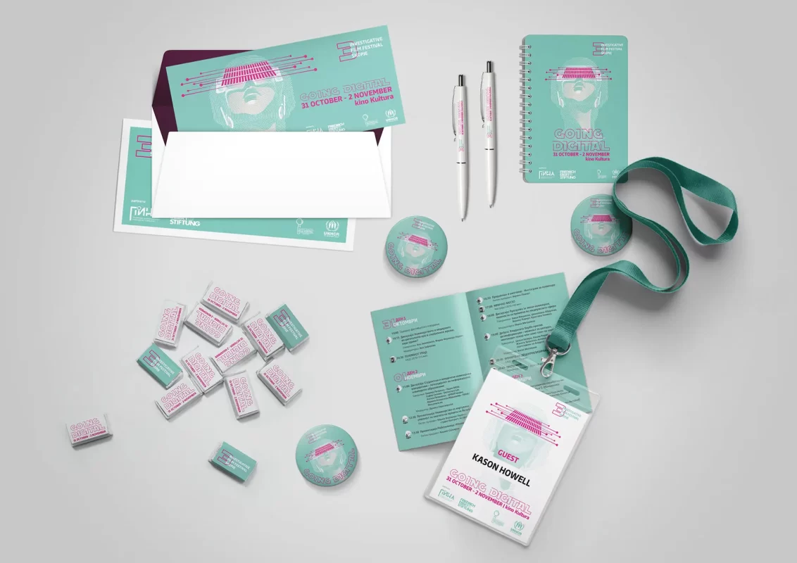 Assorted branded event materials including a badge, pens, brochure, and notepad.