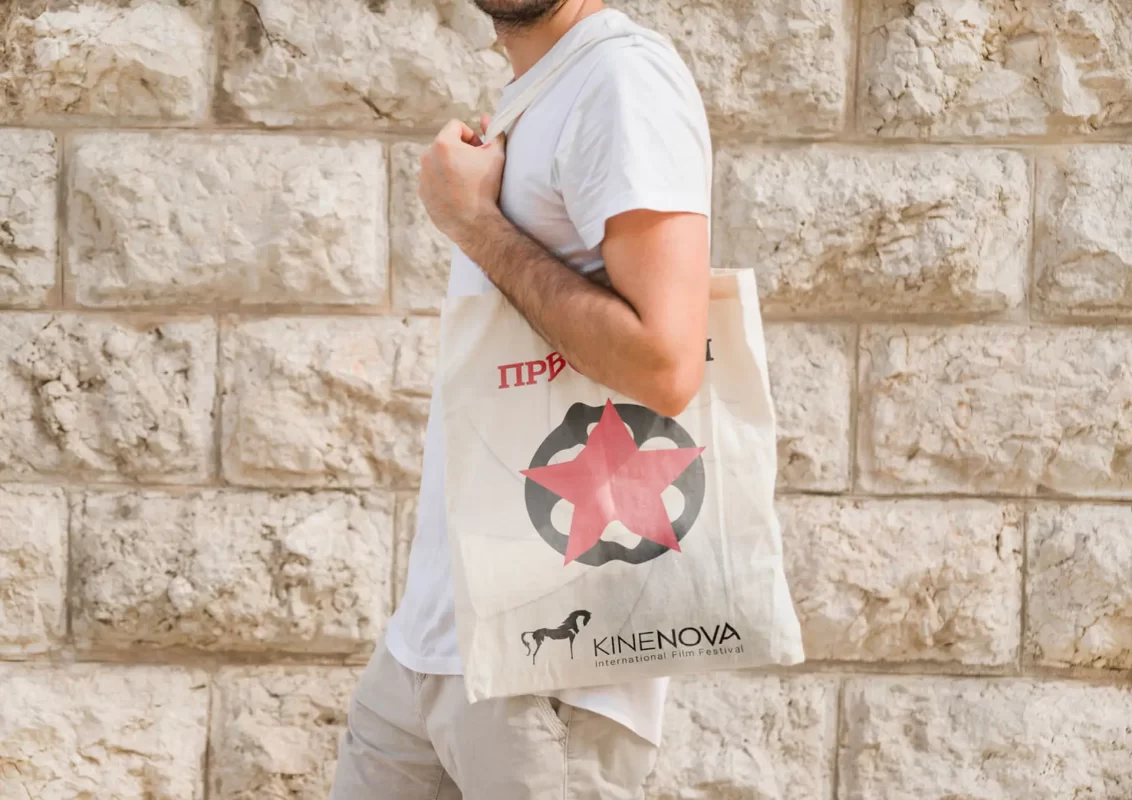 Person holding a tote bag with a graphic in front of a stone wall.