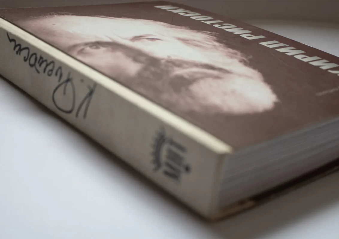 Close-up of a worn book with an obscured title and a portrait on the cover, on a white surface.