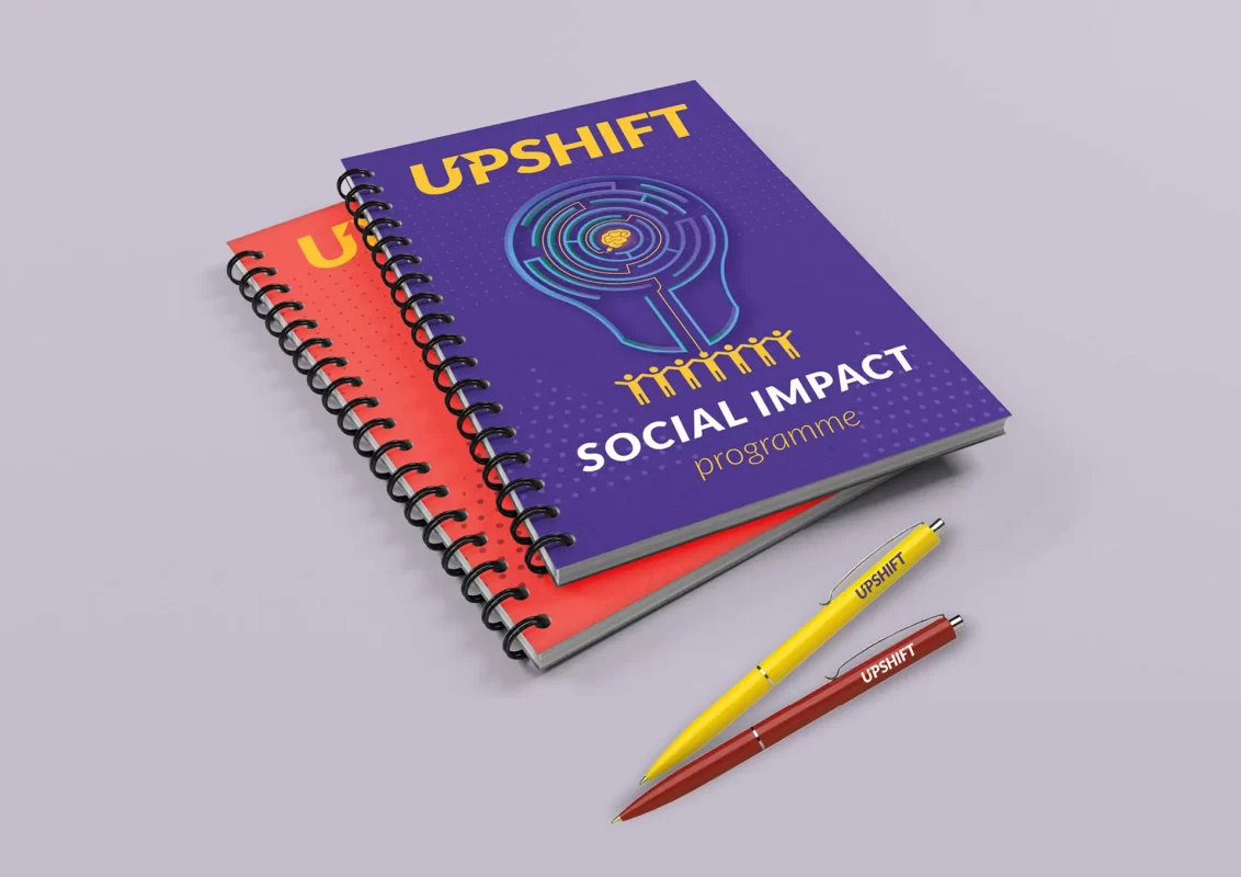 Two spiral notebooks with "UPSHIFT Social Impact" branding and two pens.