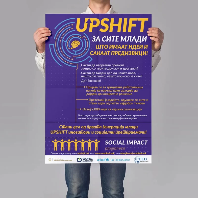 A person holding a promotional poster for an 'UPSHIFT' youth ideas and innovation program.